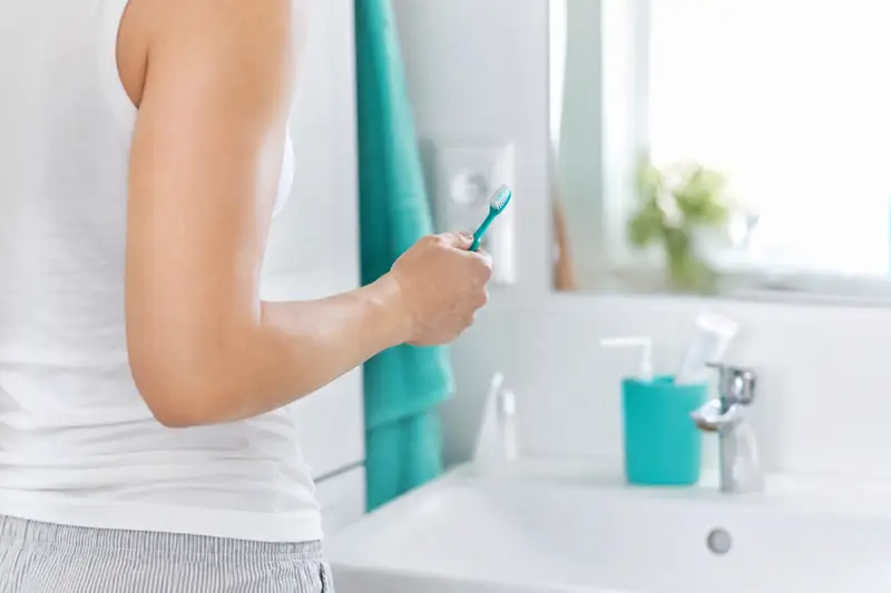Personne se brossant les dents devant un miroir de salle de bain lumineuse
