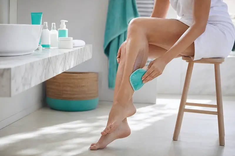 Application d’un autobronzant jambes au gant dans une salle de bains lumineuse