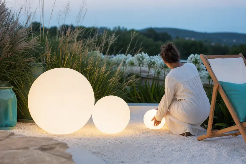 Boules lumineuses de jardin blanches éclairant une terrasse végétalisée au crépuscule.