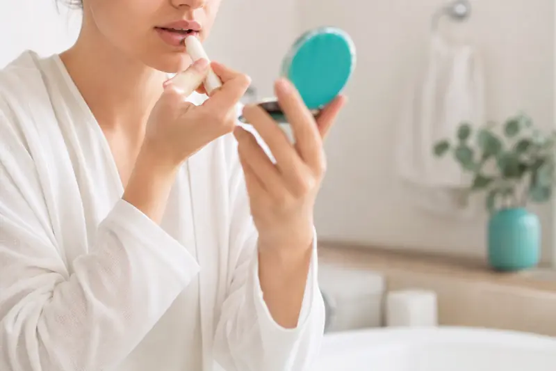 Personne appliquant un soin labial avec un miroir de poche à la main