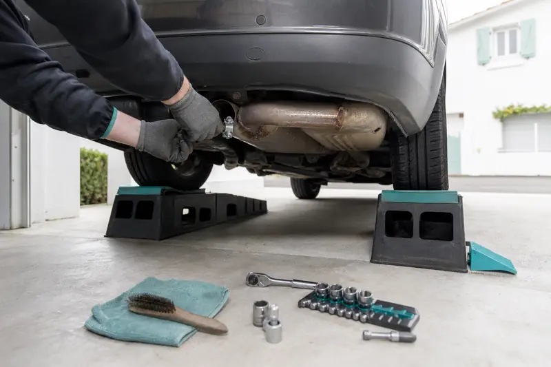 Inspection d’un échappement auto rouillé sous une voiture sécurisée sur rampes.