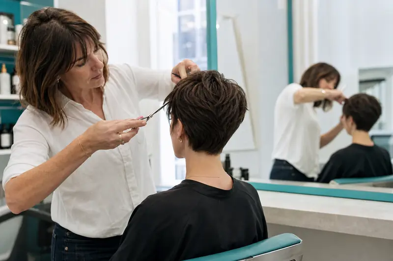 Coiffeuse ajustant une coupe de cheveux courts devant un miroir de salon.