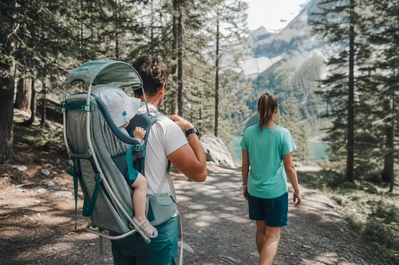 Parent réglant un porte-bébé de randonnée avec enfant sur un sentier alpin