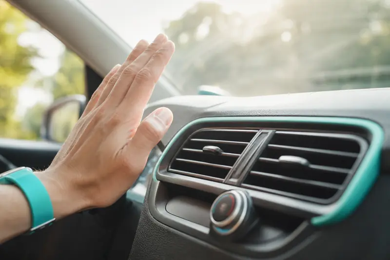 Main placée devant une bouche d'aération du tableau de bord d'une voiture en plein été