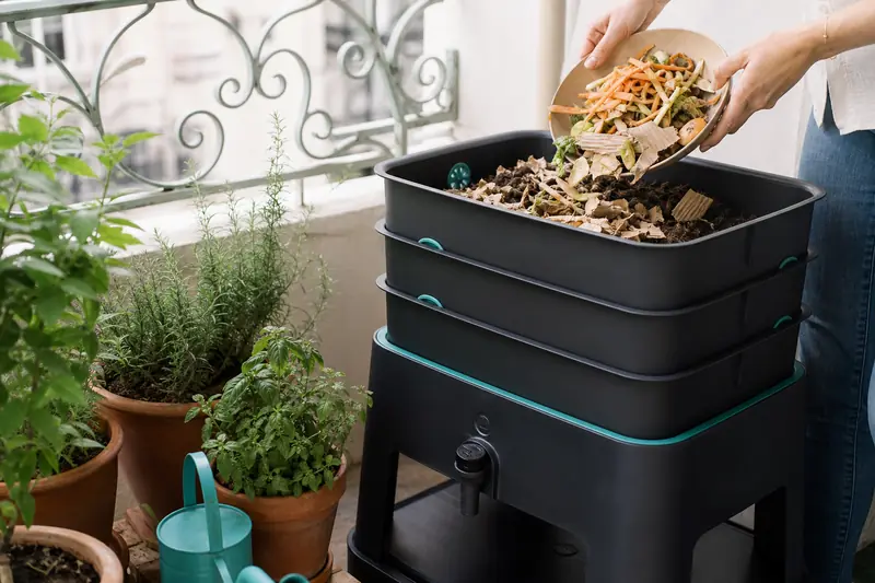 Composteur de balcon alimenté avec des épluchures près de jardinières fleuries