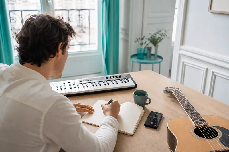 Création d’une chanson avec carnet, clavier et guitare sur une table claire