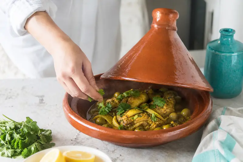 Un tajine de poulet aux olives mijote dans un plat en terre cuite.