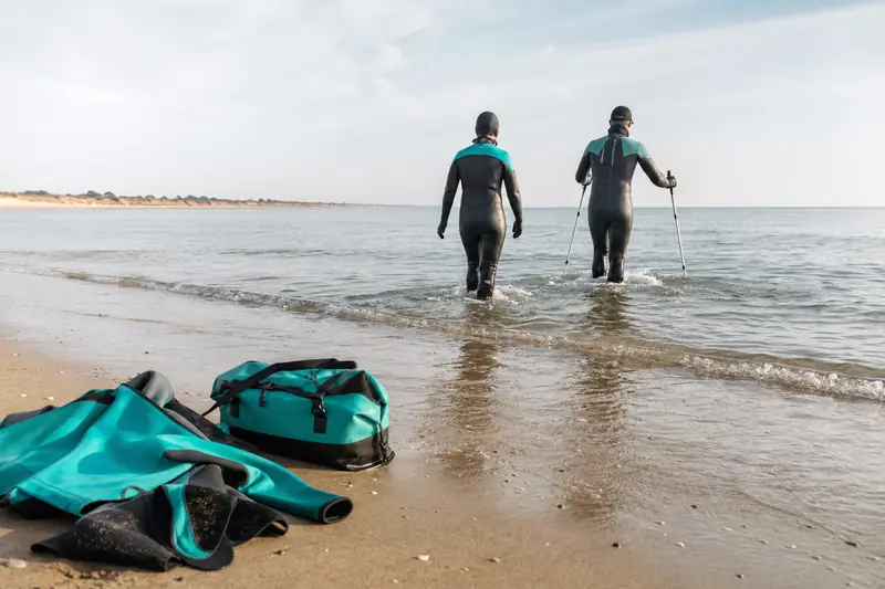 Pratiquants de longe côte en hiver marchant dans une mer calme.