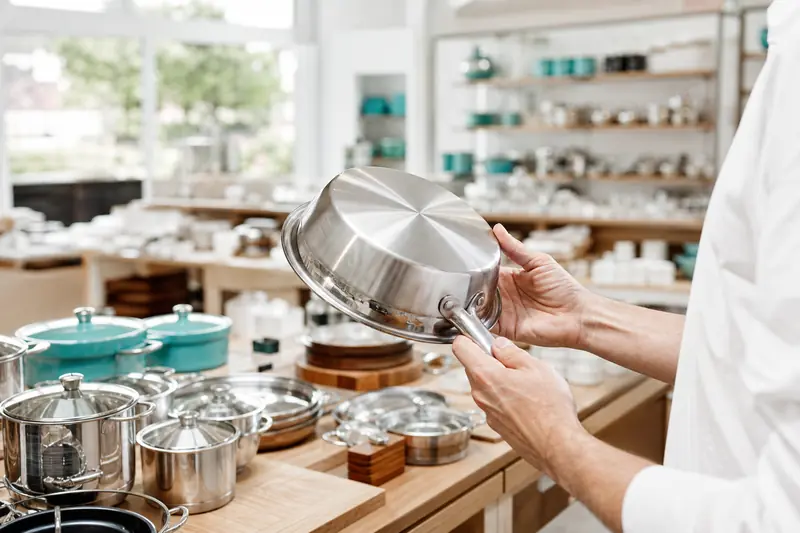Client inspectant une poêle lors d’une liquidation d’ustensiles de cuisine.
