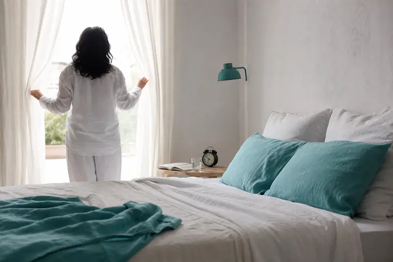 Personne ouvrant les rideaux le matin pour reprendre un rythme de sommeil régulier.