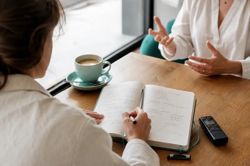 Rédacteur prenant des notes structurées pendant un entretien professionnel en café.