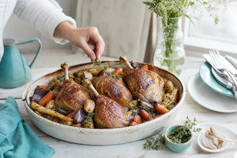 Confit de canard croustillant servi avec pommes de terre et légumes rôtis de saison.