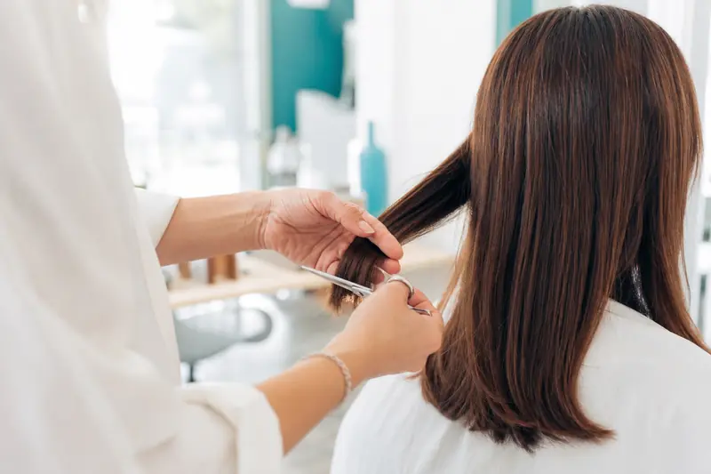 Coiffeur réalisant une coupe slide sur des mèches châtaines mi-longues.