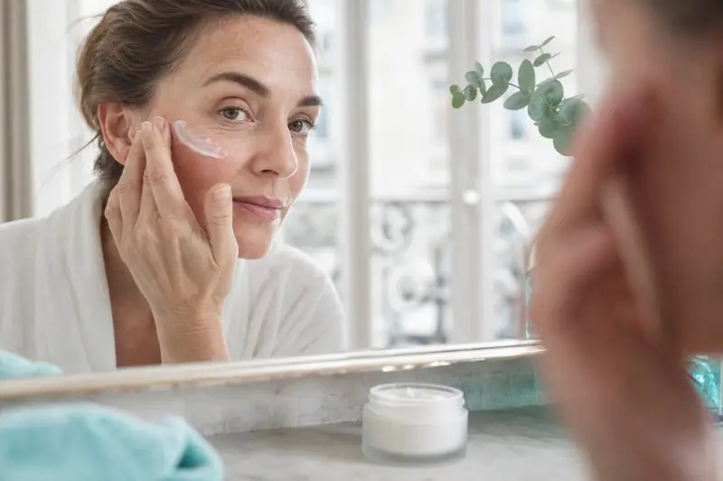 Application d’une crème anti rides bio sur le visage devant un miroir.
