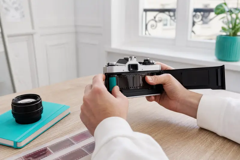 Chargement d’une pellicule dans un appareil photo argentique sur une table claire.