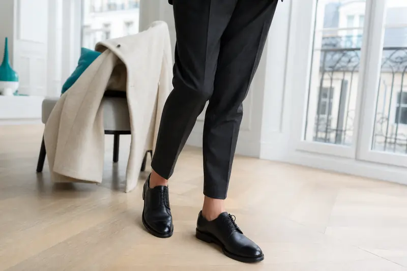 Chaussures derbi femme noires portées avec un pantalon de tailleur gris.