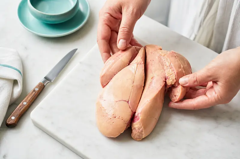 Déveinage délicat d’un foie gras cru sur une planche en marbre.