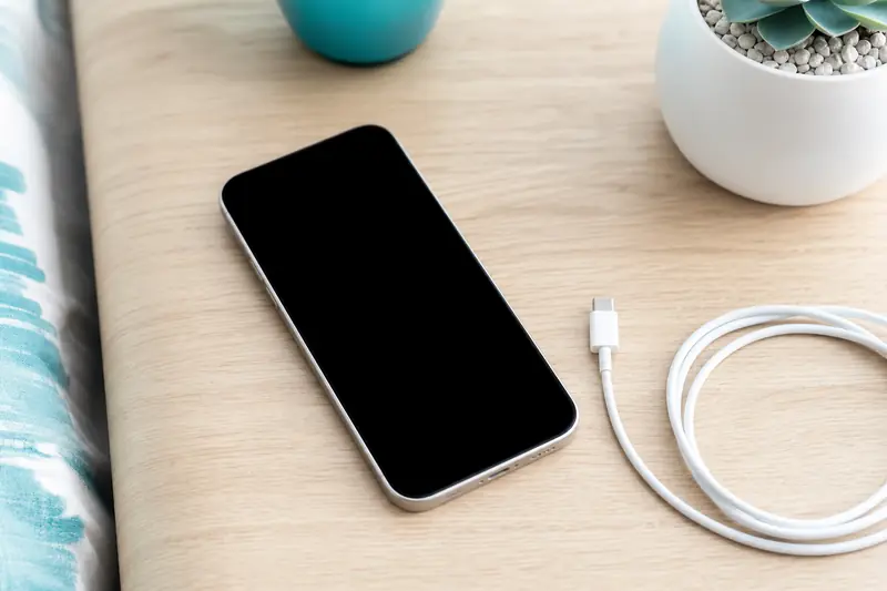 Smartphone à l'écran éteint posé sur une table à côté d'un chargeur
