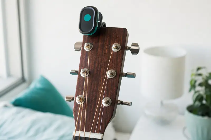 Guitare acoustique posée sur un support avec un accordeur électronique fixé à la tête