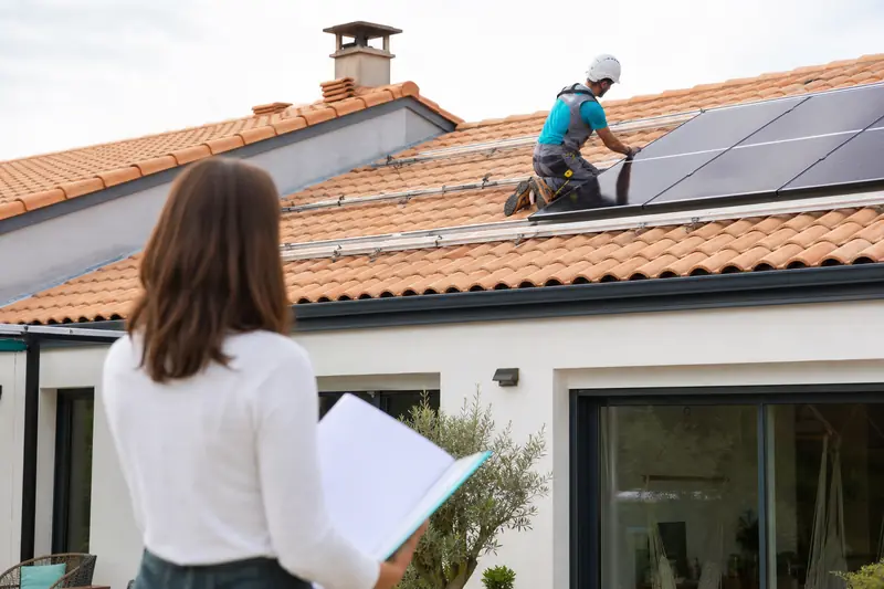Installateur solaire inspectant des panneaux photovoltaïques sur le toit d’une maison française