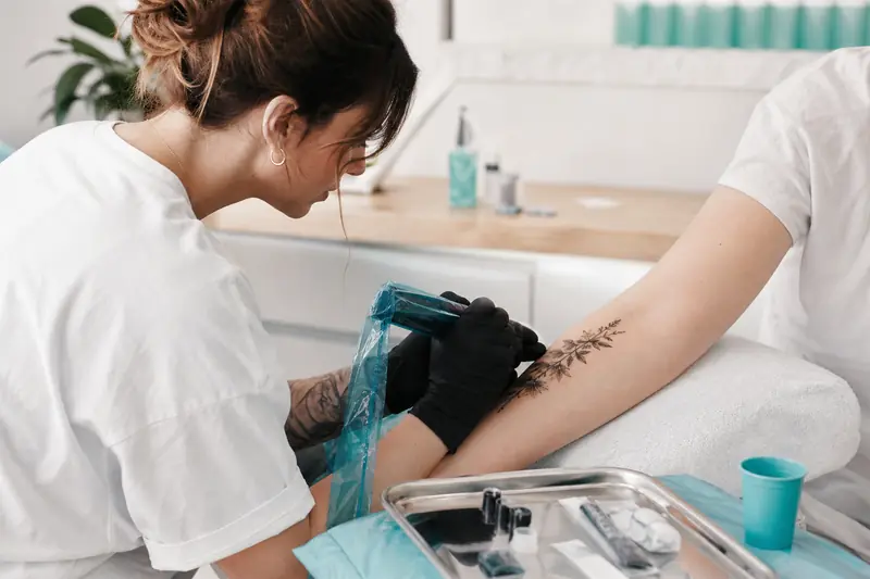 Tatoueur réalisant un tatouage botanique délicat sur un avant-bras en studio.