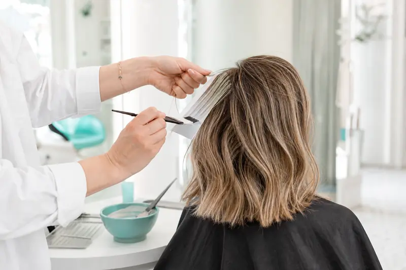 Coloriste appliquant de fines mèches de blond clair sur une cliente en salon.