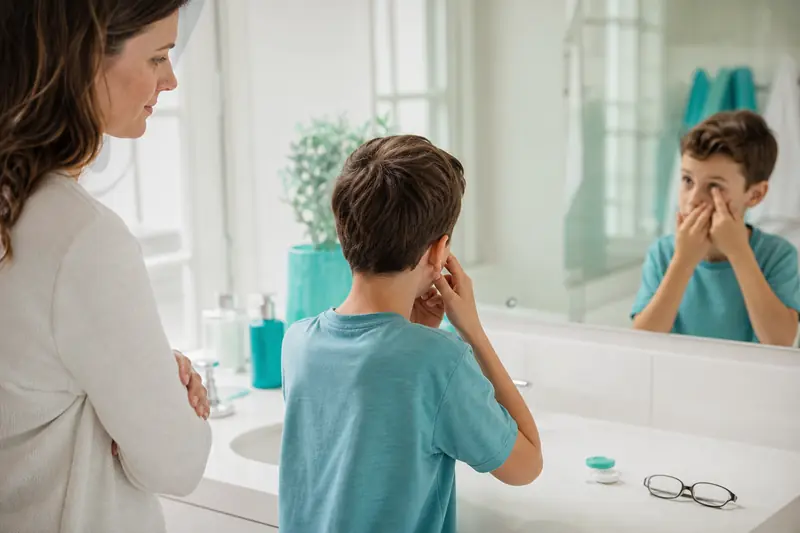 Enfant posant une lentille de contact devant un miroir avec un parent