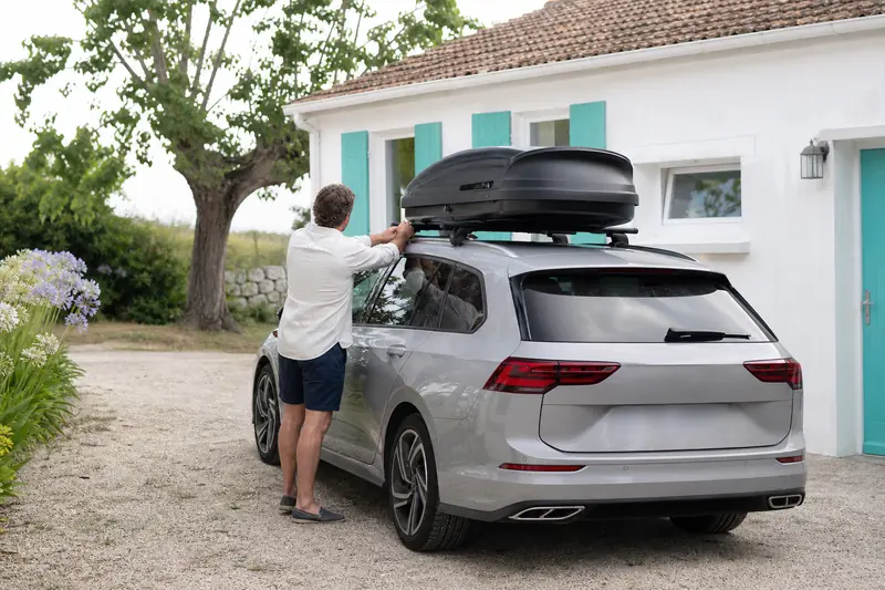 Coffre de toit fixé sur des barres au-dessus d’un toit panoramique fermé.
