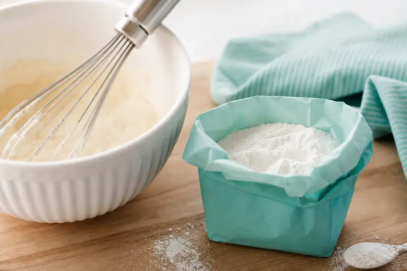Sachet de levure chimique ouvert posé sur un plan de travail avec des ustensiles de pâtisserie