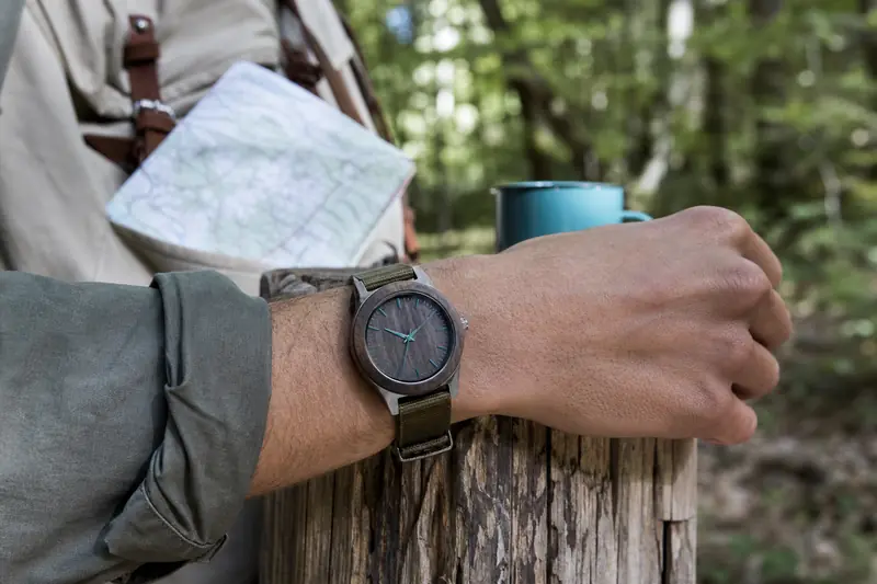 Montre en bois robuste au poignet d’un randonneur sur un sentier forestier