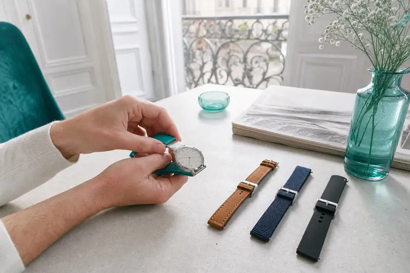 Une montre à bracelet interchangeable entourée de bracelets cuir, textile et caoutchouc.