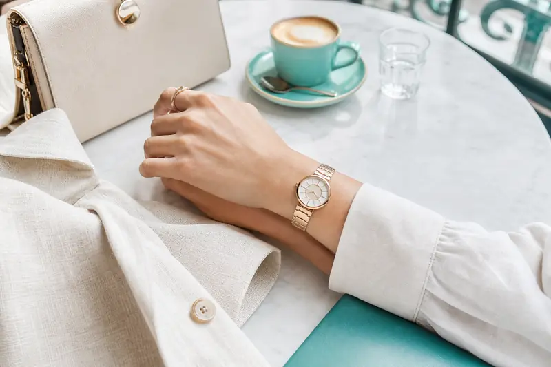 Montre Marc Jacobs femme dorée portée avec accessoires élégants sur une table de café.