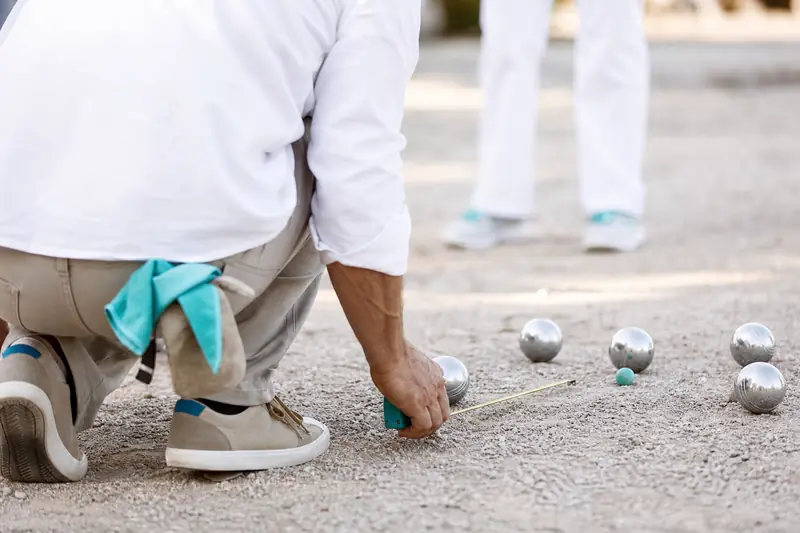 Joueur mesurant des boules lors d’une partie de pétanque compétitive sur gravier