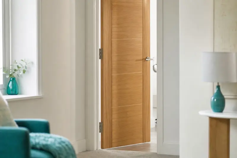 Porte intérieure en bois entrouverte avec ses gonds visibles dans un couloir lumineux