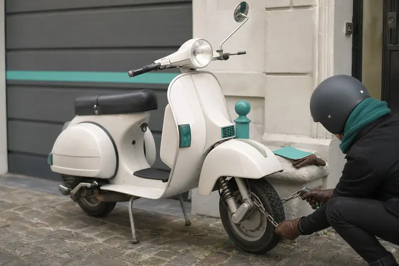 Vespa PX 125 sécurisée devant un garage avec antivol et documents d’assurance
