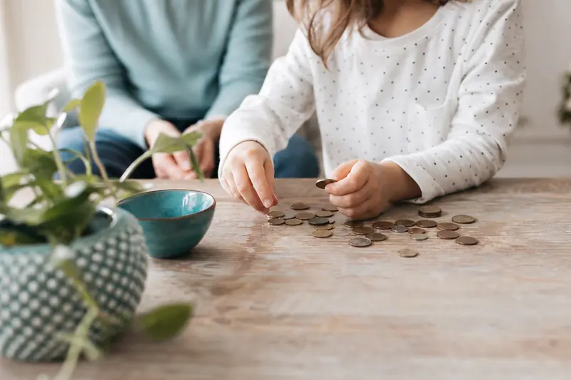 Enfant comptant des pièces de monnaie sur une table avec un parent à proximité