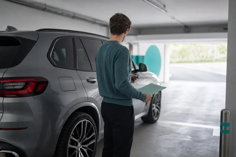 Jeune conducteur près d'une BMW X5 dans un garage sécurisé.