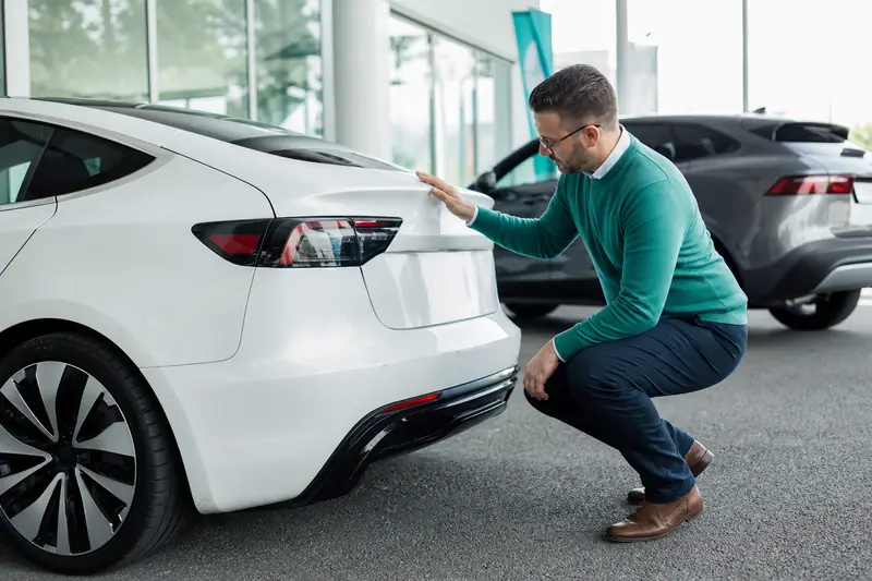 Acheteur inspectant une Tesla d’occasion sur un parking de concessionnaire.