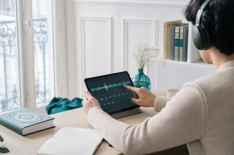 Apprentissage du Coran en ligne sur tablette, avec livre fermé et écouteurs.