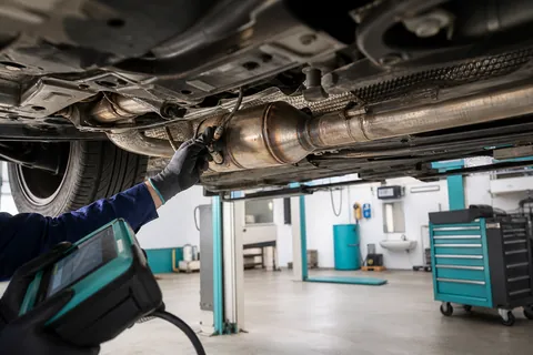 Mécanicien inspectant le catalyseur essence et une sonde lambda sous une voiture