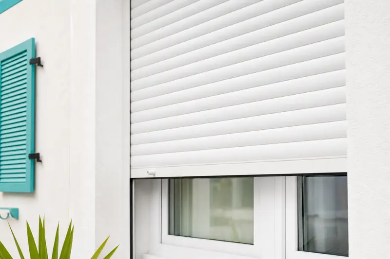 Volet roulant électrique blanc à moitié fermé sur une fenêtre de maison